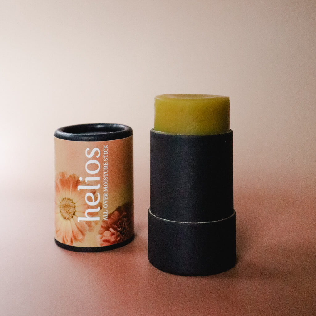 An opened black paper tube of Helios All-Over Moisture Stick herbal salve with a peach-colored floral label