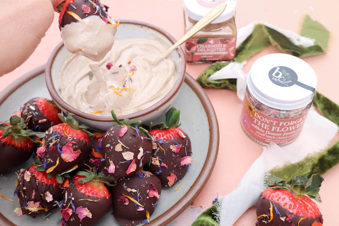 a plate of chocolate covered strawberries sprinkled with edible flower confetti with a bowl of creamy dipping sauce