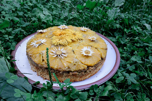 orange upside down cake decorated with edible flowers on a ceramic plate sitting in a bed of clover