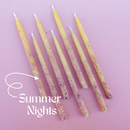 Dressed hand-dipped botanical beeswax candles rolled in powdered pink edible flowers on a pink background, labeled 'Summer Nights'.
