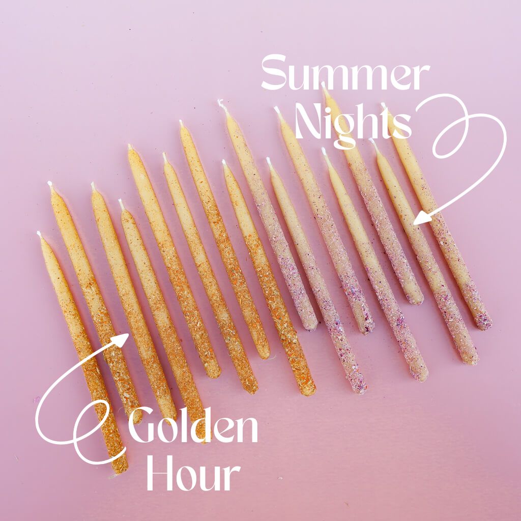 Dressed hand-dipped beeswax candles rolled in powered orange and pink edible flowers on a pink background, labeled 'Summer Nights and Golden Hour'.