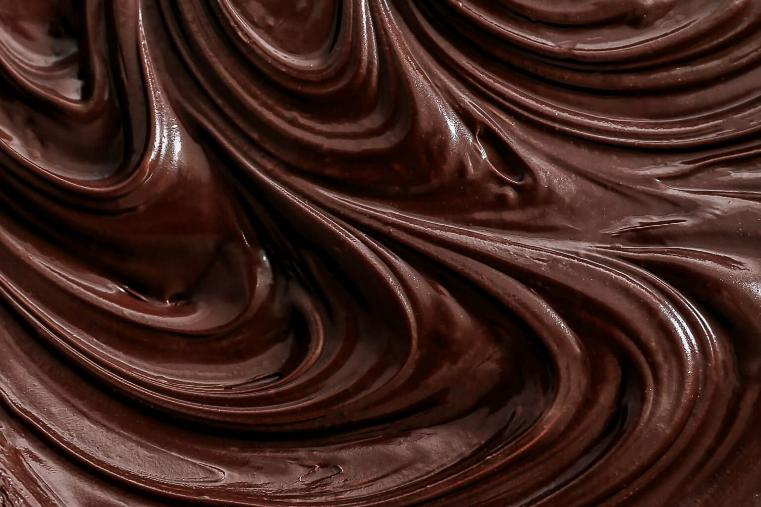 Close-up of smooth, dark chocolate frosting with swirling patterns.