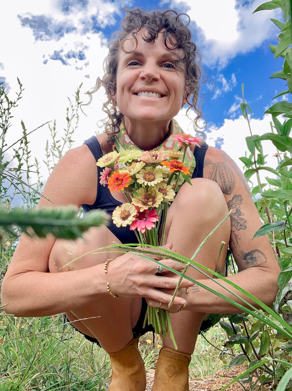 Sass Ayres, founder of Botany Culture Co.,  holding a bouquet of flowers in a natural setting with a blue sky.