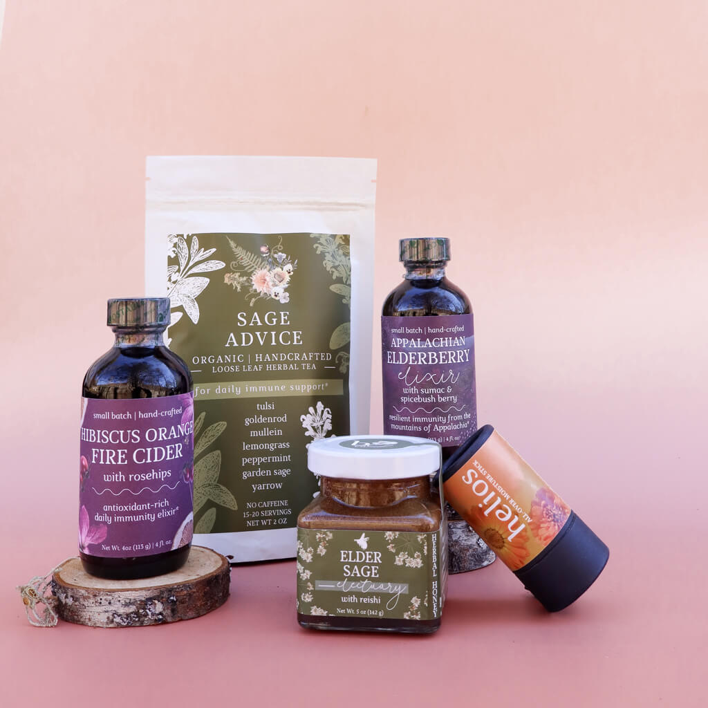 A collection of 5 Herbal products including a bag of loose-leaf herbal tea, bottles of elderberry syrup and fire cider, a jar of herbal honey, and a skin-soothing herbal salve on a pink background with dried flowers.