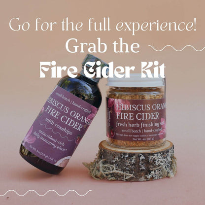 Hibiscus Orange Fire Cider bottle and a glass jar of Hibiscus Orange Fire Cider Finishing Salt on a wooden block with text overlay that reads "Go for the full experience! Grab the fire cider kit." on a pink background