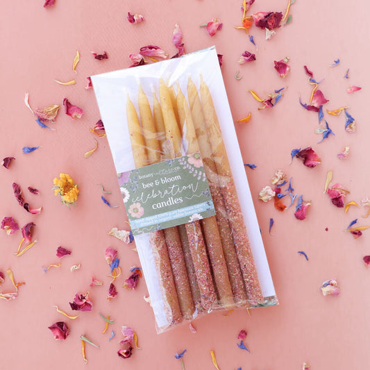 Pack of birthday-style hand-dipped beeswas candles with a decorative label on a pink background with edible flower confetti.