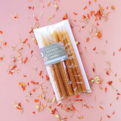 Pack of birthday-style hand-dipped beeswas candles with a decorative label on a pink background with floral confetti.