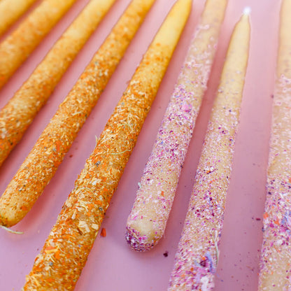 Two types of botanical beeswax birthday candles rolled in powered edible flowers on a pink background