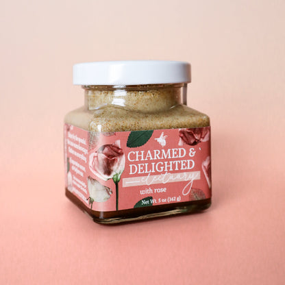 A jar of Charmed and Delighted herbal honey for heart, cardiovascular, and emotional health against a moody light pink gradient background.