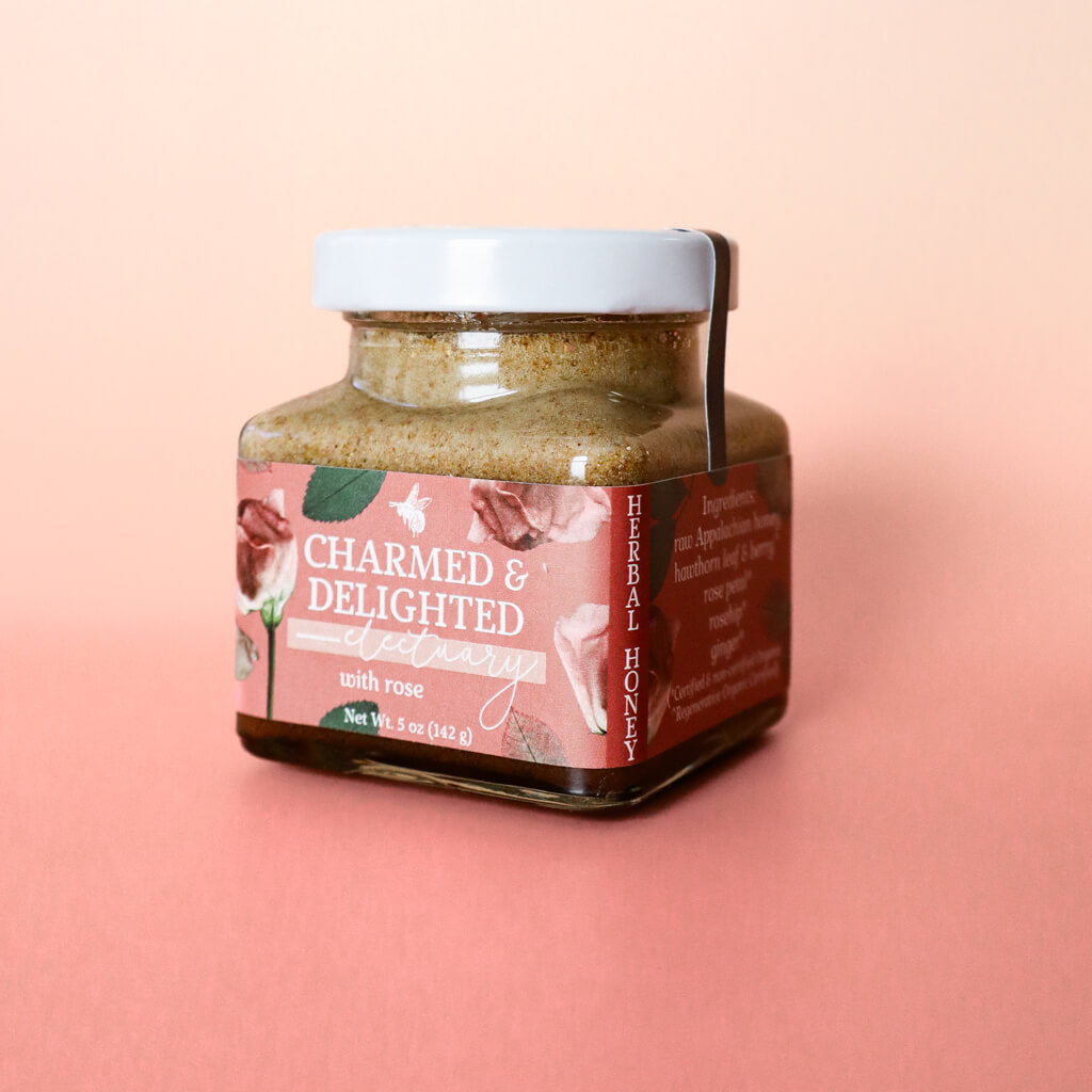 A jar of Charmed and Delighted herbal honey for heart, cardiovascular, and emotional health against a moody light pink gradient background.