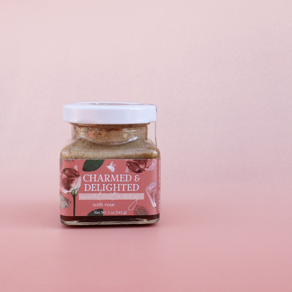 Jar of 'Charmed & Delighted Herbal Honey with Rose' product on a pink background