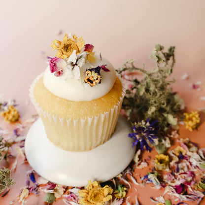A vanilla cupcake with vanilla frosting decorated with dried edible flowers