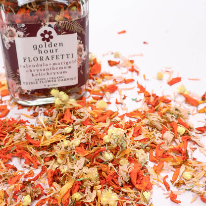 Bottle of Golden Hour Florafetti Edible Dried Flower Garnish with scattered orange and yellow edible flowers on a white background