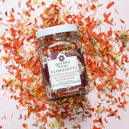 Jar of Golden Hour Florafetti Edible Dried Flower Garnish with scattered orange and yellow edible flowers on a white background
