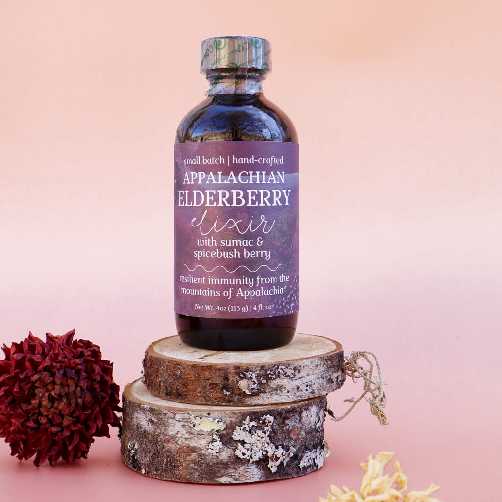 Bottle of Appalachian Elderberry Elixir for Immune Support on a wooden log with a pink background