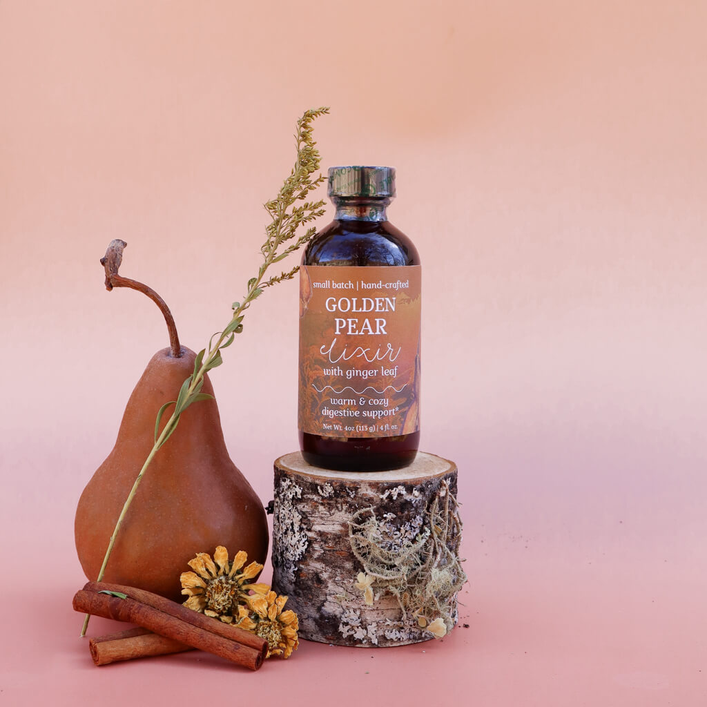 Bottle of 'Golden Pear Elixir: Warming Digestive Support' with a pear, cinnamon sticks, and flowers on a pink background
