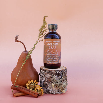 Bottle of 'Golden Pear Elixir: Warming Digestive Support' with a pear, cinnamon sticks, and flowers on a pink background