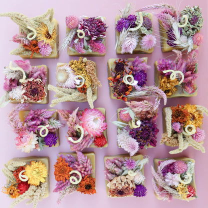Aerial view of a bunch of square-shaped beeswax fire starters with dried flowers embedded in them against a light pink background