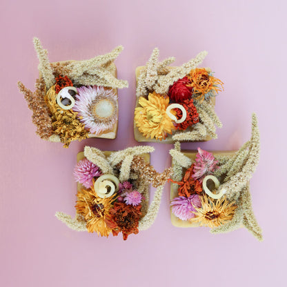 Aerial view of 4 square-shaped beeswax fire starters with dried flowers embedded in them against a light pink background
