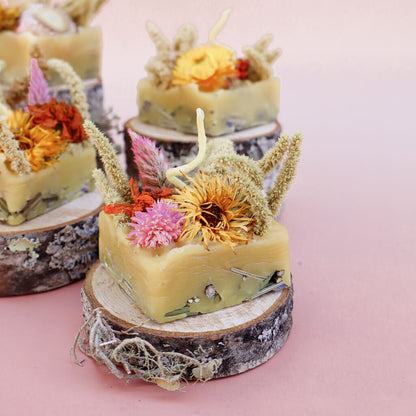 A square-shaped beeswax fire starters with dried flowers embedded in it sitting on a decorative wood prop