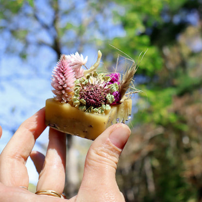 Hand holding a beeswax fire starter with a cotton wick and dried flowers against a natural background