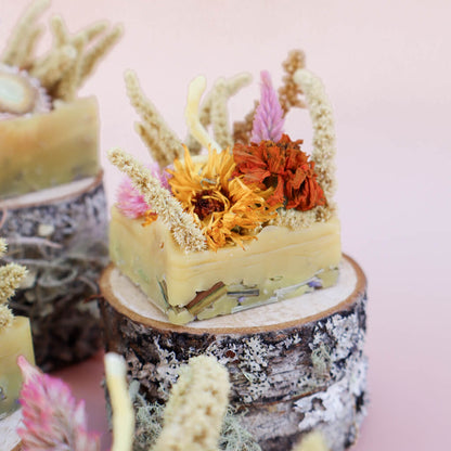 A square-shaped beeswax fire starters with dried flowers embedded in it sitting on a decorative wood prop