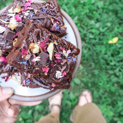Chocolate brownies decorated with edible flower finishing salt and rose petals on a plate held over grass