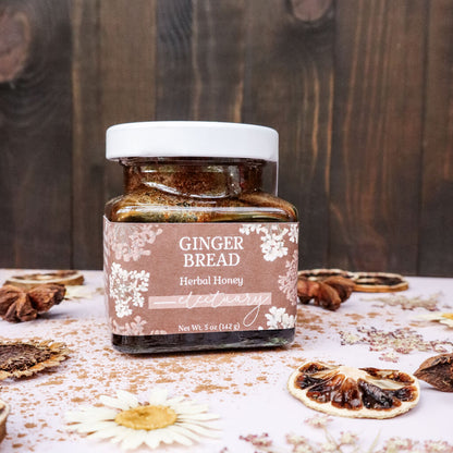 Jar of Gingerbread Herbal Honey on a wooden surface with spices and dried flowers