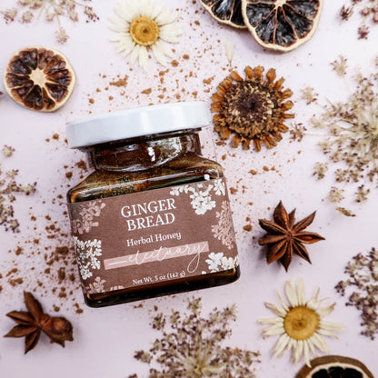 Jar of 'Gingerbread' herbal honey surrounded by dried herbs and flowers on a light background