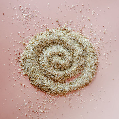 A spiral-pattered pile of Hibiscus Orange Fire Cider finishing salt with citrus spice and herbs against a light pink background.