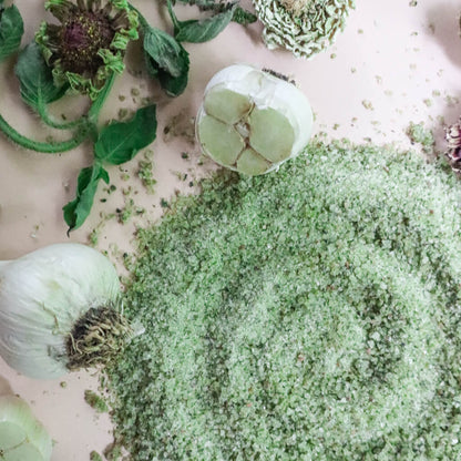 Green-colored herbal salt with garlic bulbs and leaves on a light background