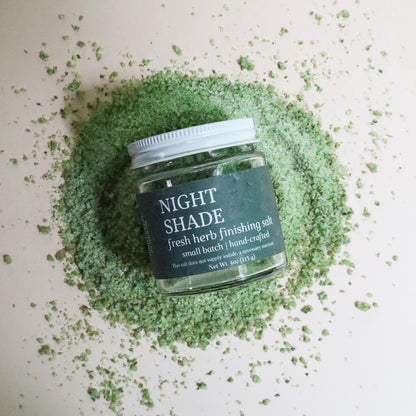 Jar of 'Night Shade' fresh herb finishing salt surrounded by green powder on a light background