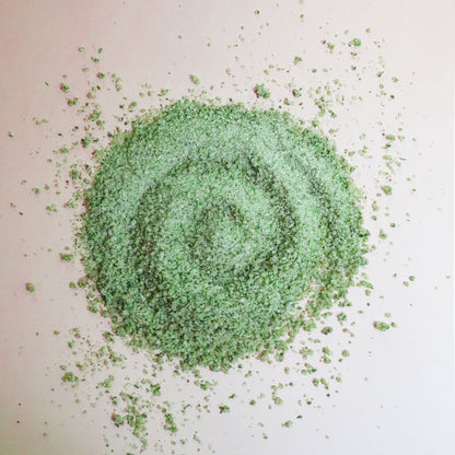 A pile of green herbal finishing salt in a circular pattern on a beige background