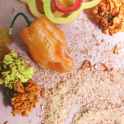 Orange chili pepper on a surface with scattered spicy salt and dried marigold flowers