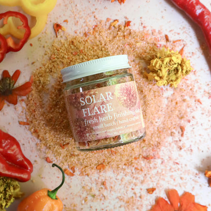 Jar of 'Solar Flare' fresh herb seasoning surrounded by spices and herbs on a textured surface.