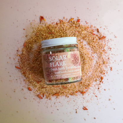 Jar of 'Solar Flare' fresh herb seasoning surrounded by spices on a white surface