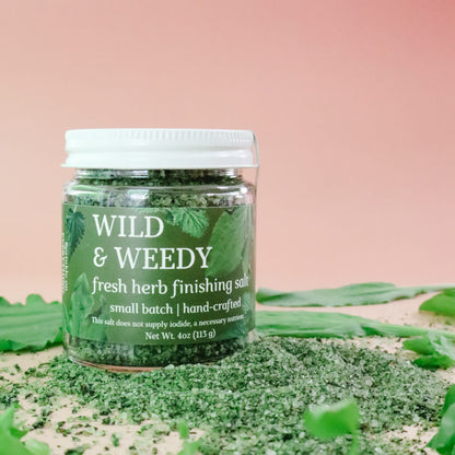 Jar of 'Wild & Weedy' fresh herb finishing salt with plantain leaves and chickweed on a pink background