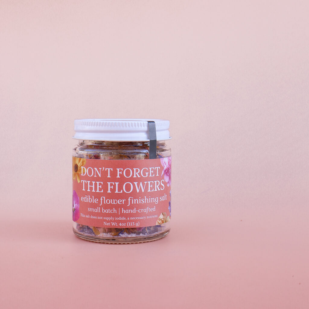 Jar of 'Don't Forget the Flowers' edible flower finishing salt on a pink background
