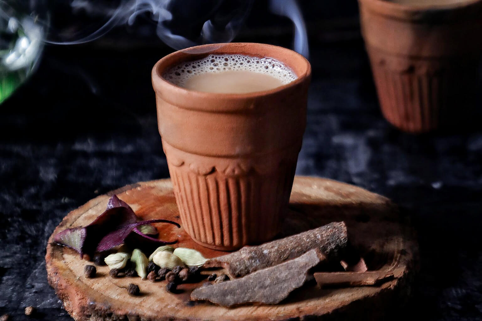Terracotta cup with steaming chai beverage on a wooden coaster with spices