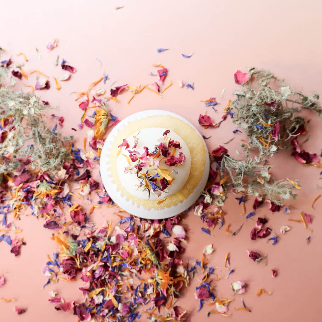 Aerial view of a cupcake decorated with colorful dried organic edible flowers on a pink background