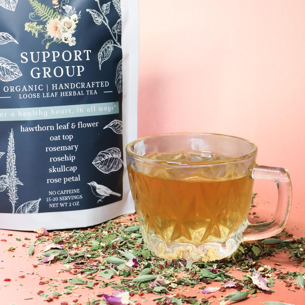 Loose leaf tea packaging labeled 'Support Group: For a Healthy Heart' with a glass of tea and tea leaves on a pink background