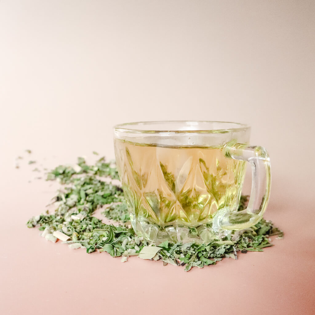 A clear cup of organic herbal tea, placed on a table with scattered organic loose-leaf around