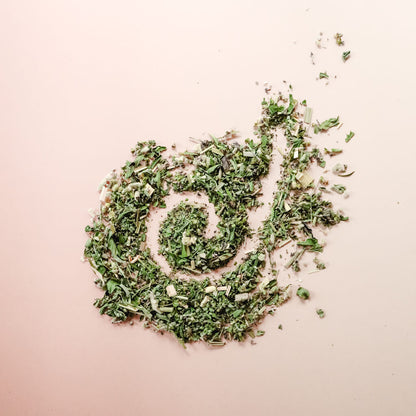 A pile of organic loose-leaf tea with a spiral pattern through it on a light pink background