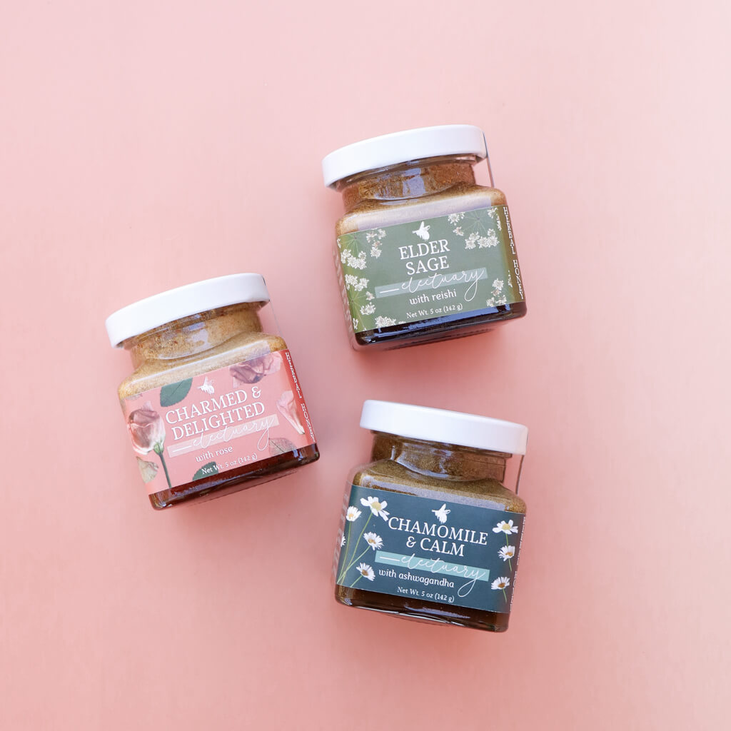 Three jars of different herbal honeys on a pink background
