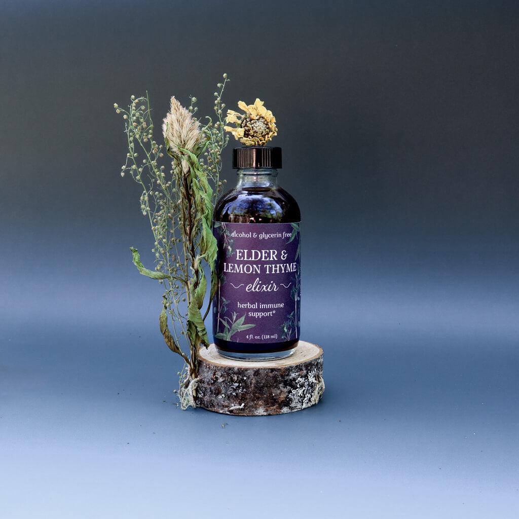 Bottle of 'Elder & Lemon Thyme Elixir' on a wooden stand with decorative elements against a gradient background