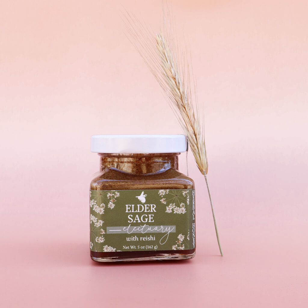 Jar of sage and elderflower honey with Reishi with a decorative plant on a pink background