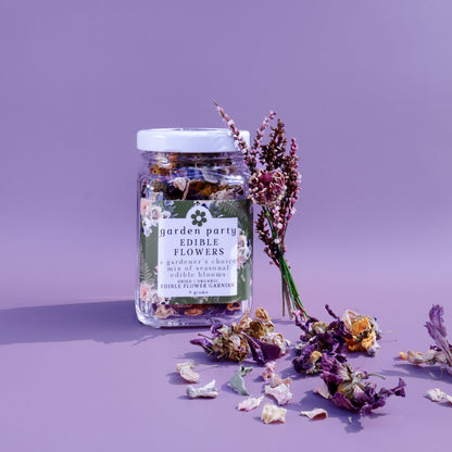 a jar of Garden Party Edible Flowers: Dried Organic Edible Flower Garnish against a purple background with dried edible flowers scattered in front