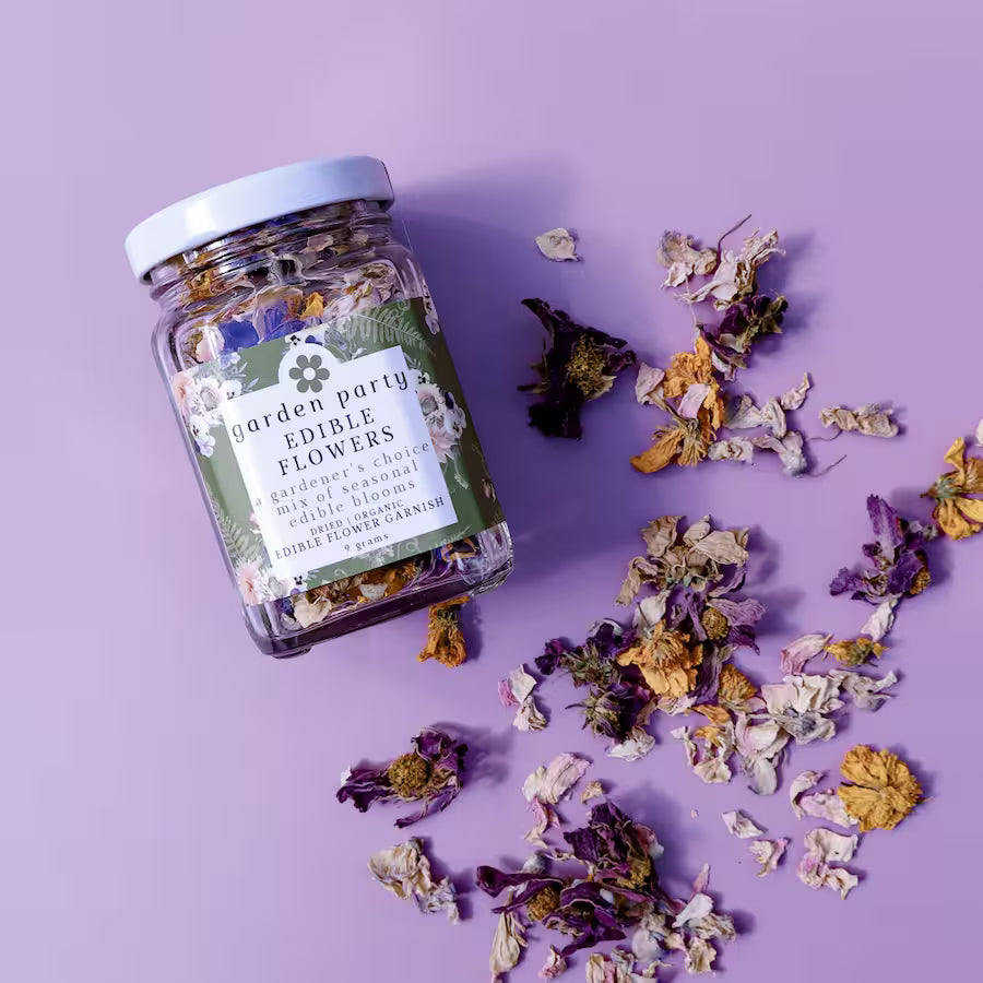 a jar of Garden Party Edible Flowers: Dried Organic Edible Flower Garnish against a purple background with dried edible flowers scattered in front