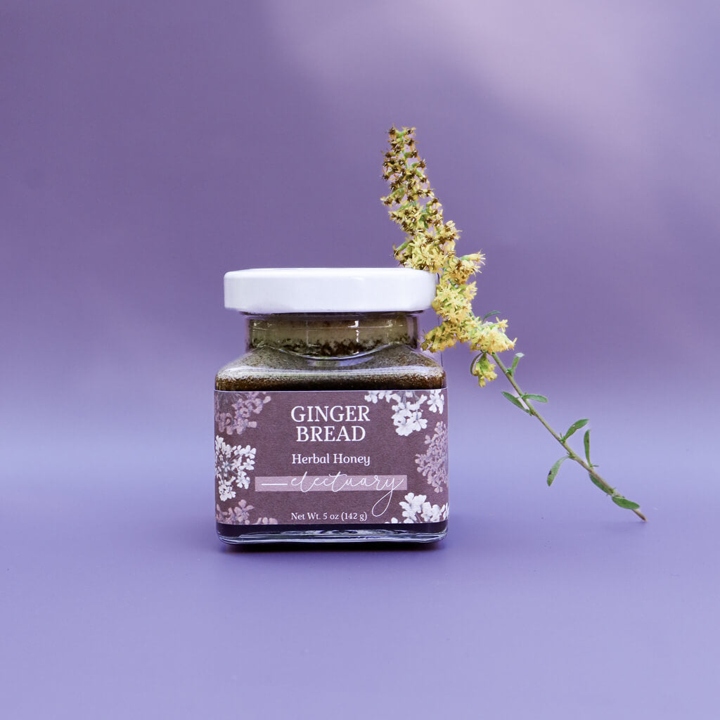 A jar of Gingerbread Herbal Honey against a purple background with a goldenrod flower leaning against it as decoration