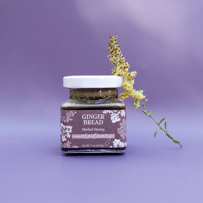 A jar of Gingerbread Herbal Honey against a purple background with a goldenrod flower leaning against it as decoration